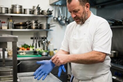 Chef professionnel en train de mettre des gants bleus dans une cuisine